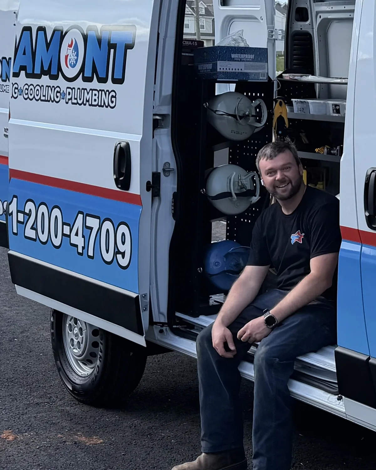 Smiling Tramont team member sitting on the step of a wrapped Tramont service van