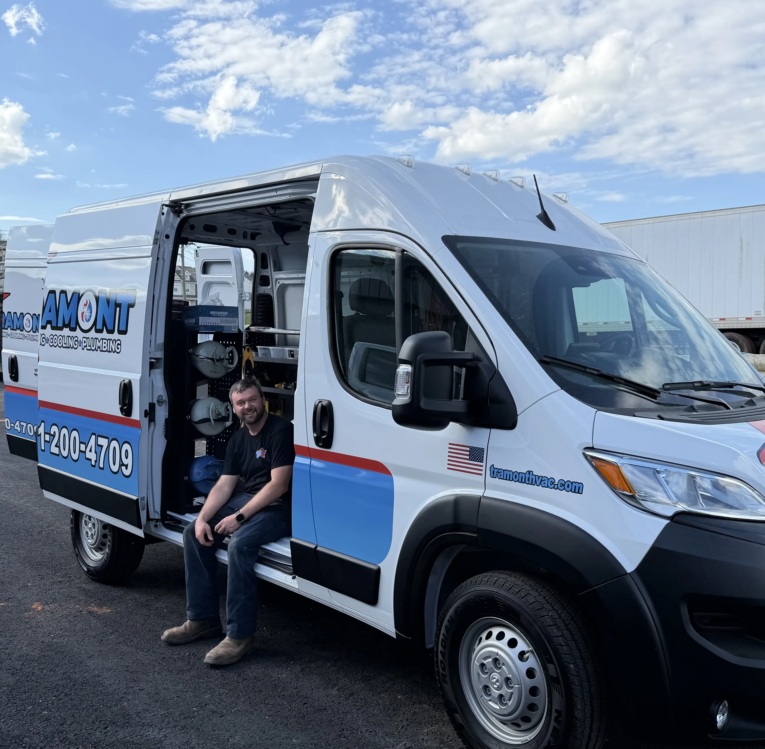 Smiling Tramont team member sitting on the step of a wrapped Tramont service van